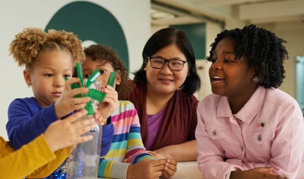 an adult supervising three young girls while they work on a science project