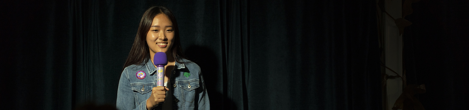  A Girl Scout stands on a stage with a microphone smiling 