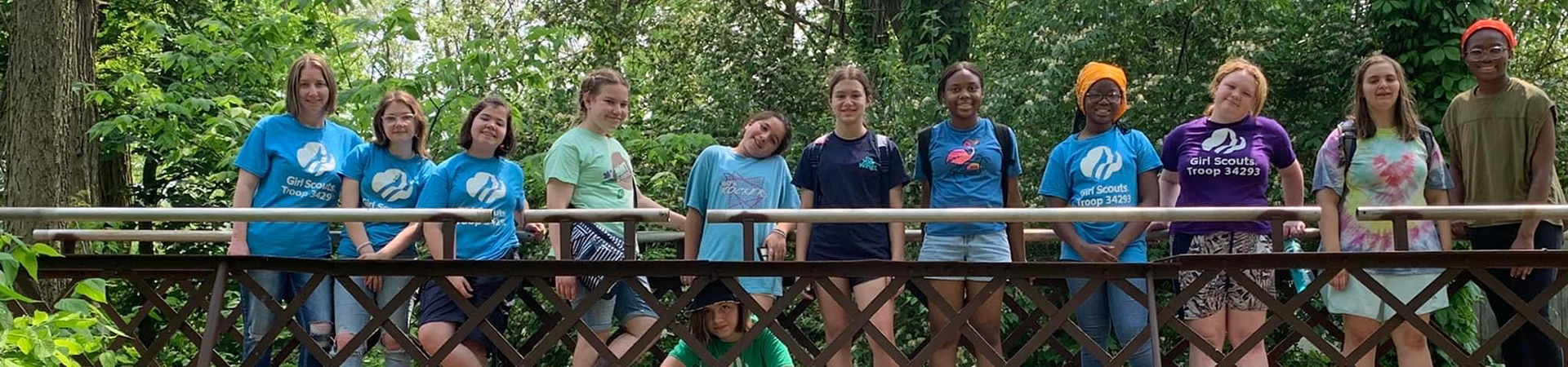  Girl Scouts standing on a bridge in the forest. 