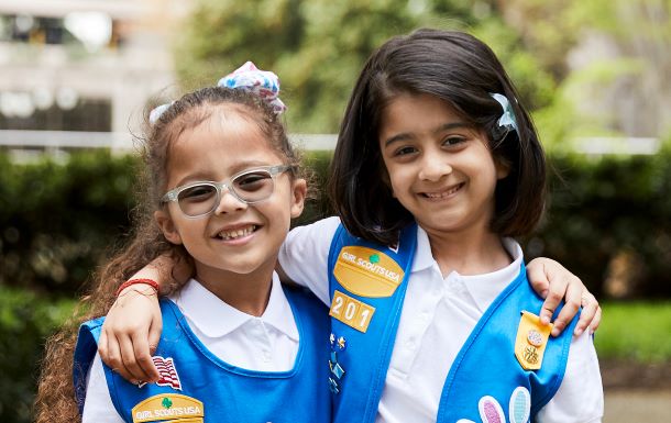 Two Daisy Girl Scouts in uniform with their arms around each other