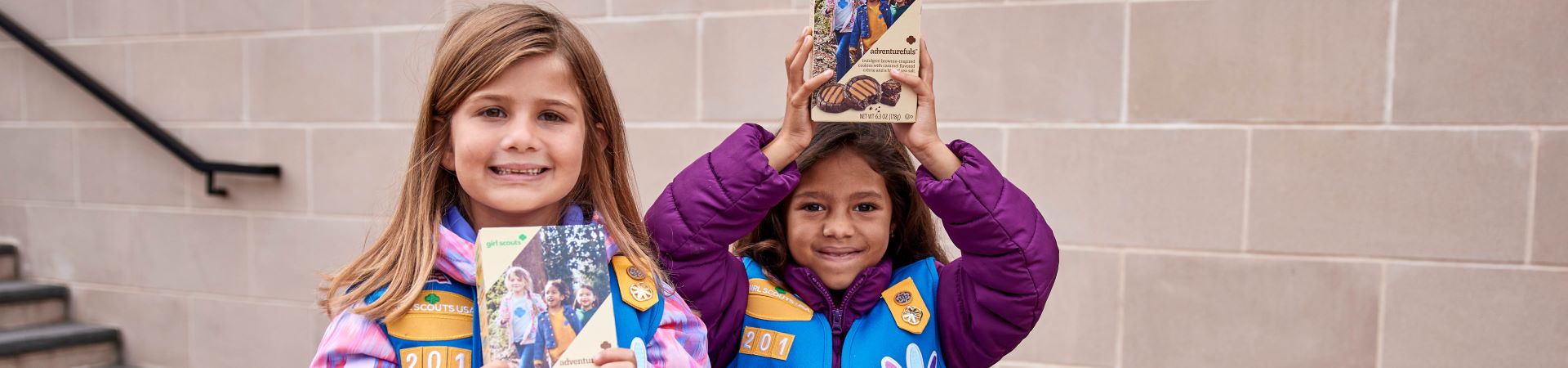  Two Girl Scouts holding boxes of cookies at a booth 