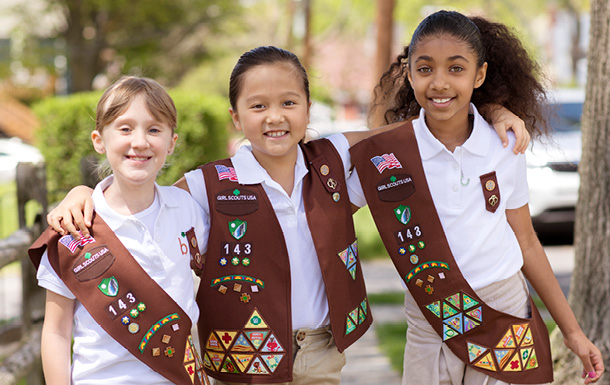 Three Girl Scouts outdoors with their arms around each other