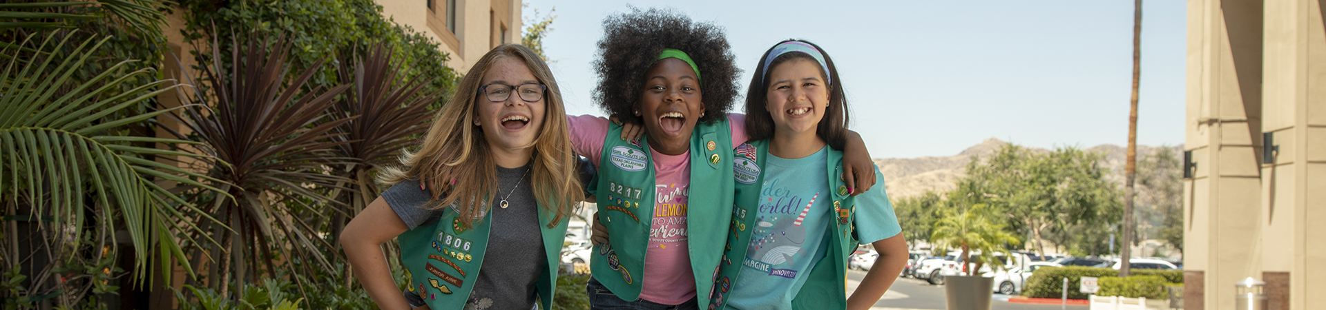  Three Girl Scout Juniors stand arm in arm smiling  