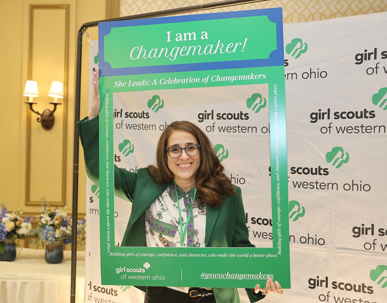 Dr. Maria Ortiz, holding "I am a Changemaker" sign in front of Girl Scouts of Western Ohio banner