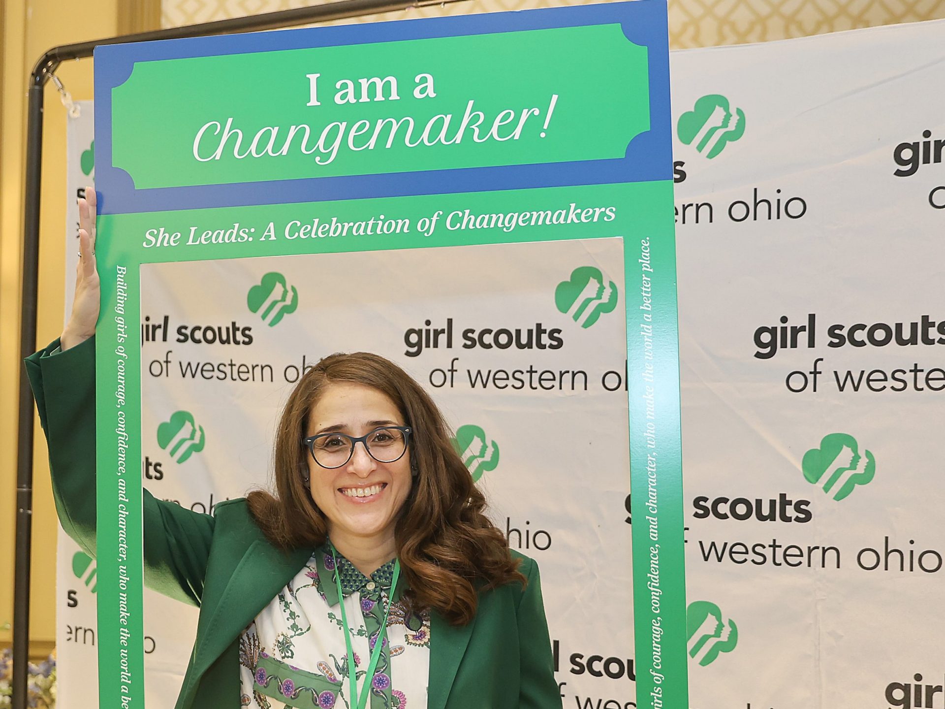 Dr. Maria Ortiz, holding "I am a Changemaker" sign in front of Girl Scouts of Western Ohio banner